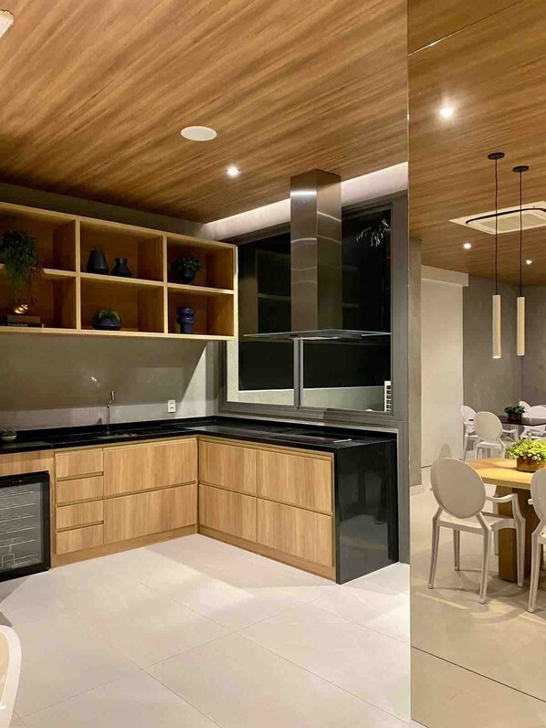 A modern kitchen with wooden cabinets, a black countertop, and a built-in stove. There is a dining area with a table and chairs.