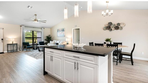 Una cocina moderna con armarios blancos, encimera negra y un comedor con mesa y sillas.