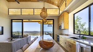 A modern kitchen with a large island, wooden cabinets, and a view of the outdoors. - La Joya De La Selva ~ An Eco-Luxury Experience (Nosara)