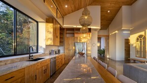 A modern kitchen with a large island, wooden cabinets, and a view of the outdoors. - La Joya De La Selva ~ An Eco-Luxury Experience (Nosara)