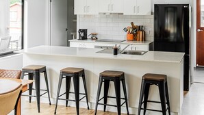 Une cuisine moderne avec des meubles blancs, un réfrigérateur noir et trois suspensions noires.