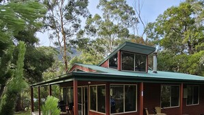 A wooden cabin with a covered porch and large windows, surrounded by lush greenery.