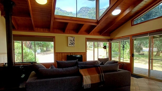 A spacious living area with a high ceiling, wooden beams, and large windows offering views of the outdoors.