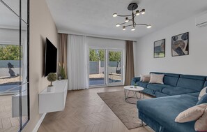 Un salón moderno con un sofá azul, un televisor de pantalla plana, una mesita y una lámpara de techo.