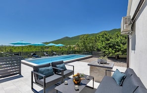 Área de piscina com espreguiçadeiras, guarda-sóis e uma mesa com frutas e bebidas.