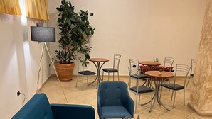 A modern living room with a blue sofa, two armchairs, a glass coffee table, and a dining area with metal chairs and a small table. - Hotel Vico Alto Siena (Siena)