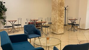 A modern lounge area with blue sofas, round glass tables, and metal chairs. - Hotel Vico Alto Siena (Siena)