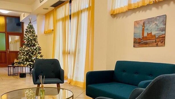 A lobby with a Christmas tree, teal sofas, and a glass coffee table. - Hotel Vico Alto Siena (Siena)