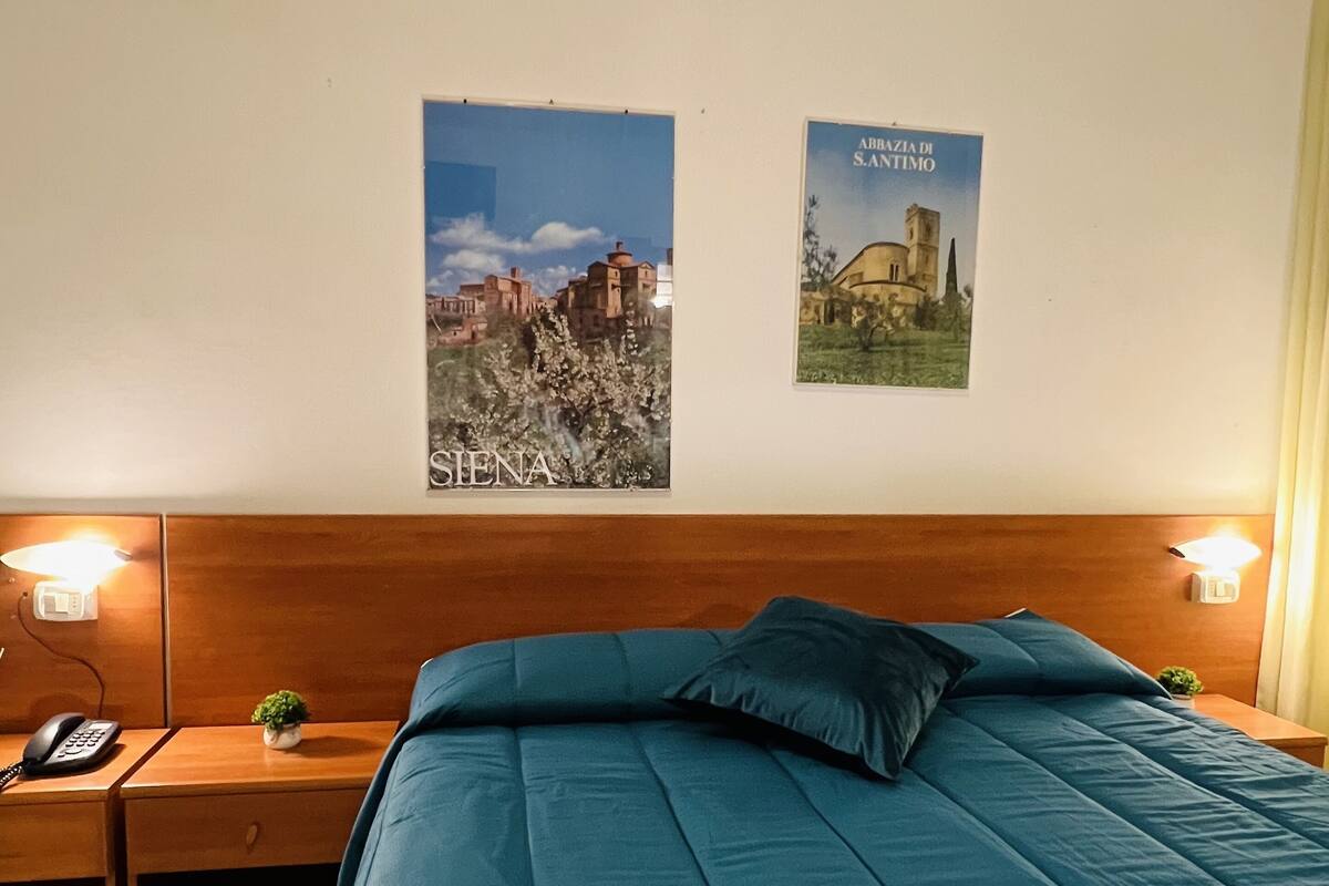 A hotel room with a large bed, wooden headboard, two bedside tables with lamps, a phone, and two framed pictures on the wall.