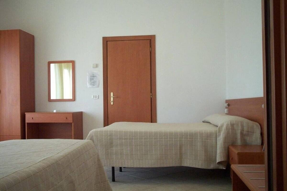 A bedroom with two beds, a wooden wardrobe, a small desk, and a door.