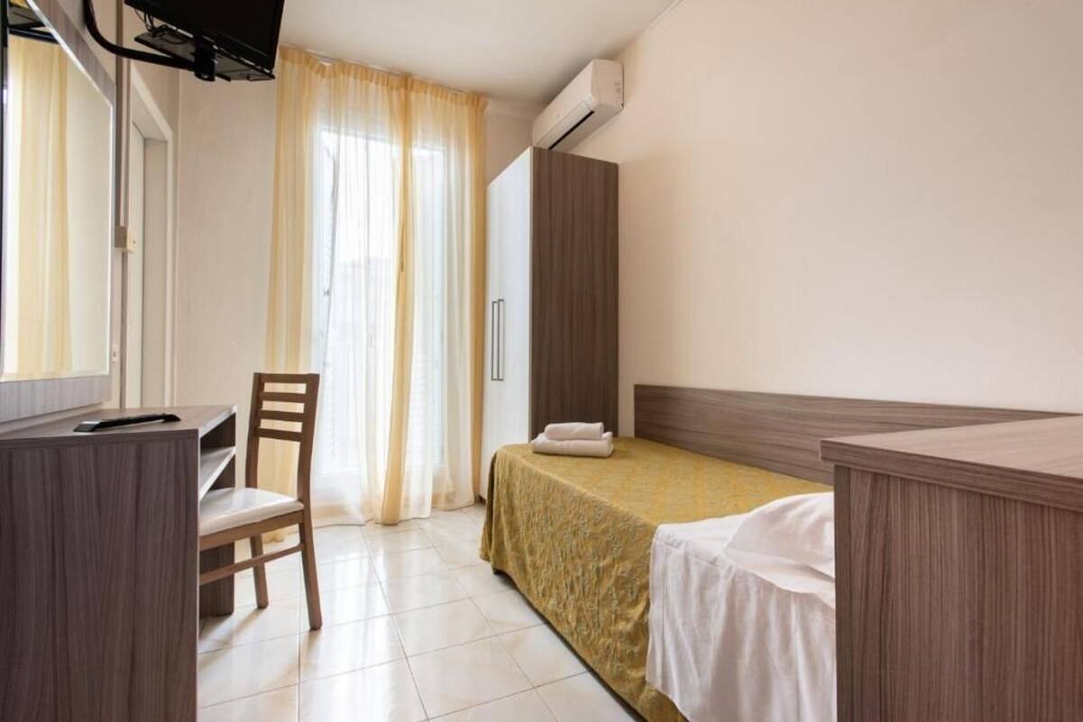 A hotel room with a bed, a desk, a chair, and a wardrobe.