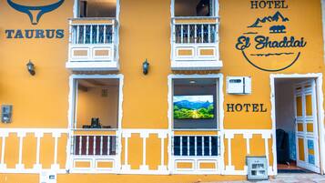 Un edificio amarillo con balcones, una pantalla de televisión y un letrero que dice "Hotel El Shaddai".