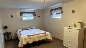 A bedroom with a bed, two windows with curtains, a bedside table with a lamp, and a dresser. - Spacious 2 bedroom apartment  (Warren)