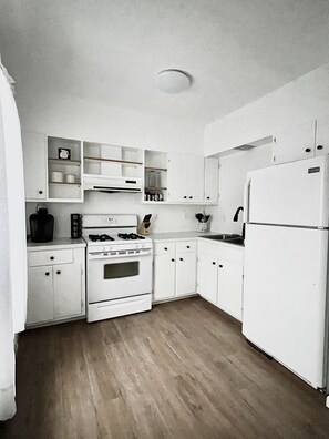 A compact kitchen with white cabinetry, a stove, a sink, and a refrigerator. - Spacious 2 bedroom apartment  (Warren)