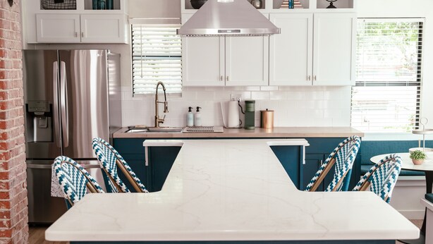 Una cocina moderna con armarios blancos, un refrigerador de acero inoxidable, una encimera de mármol y sillas azules.