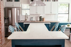 A modern kitchen with white cabinets, a stainless steel refrigerator, a marble countertop, and blue chairs. - Beautiful remodeled historical home in safe neighborhood downtown. (Oklahoma City)