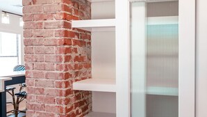 Una habitación con un pilar de ladrillo, estanterías blancas y una puerta de vidrio esmerilado.