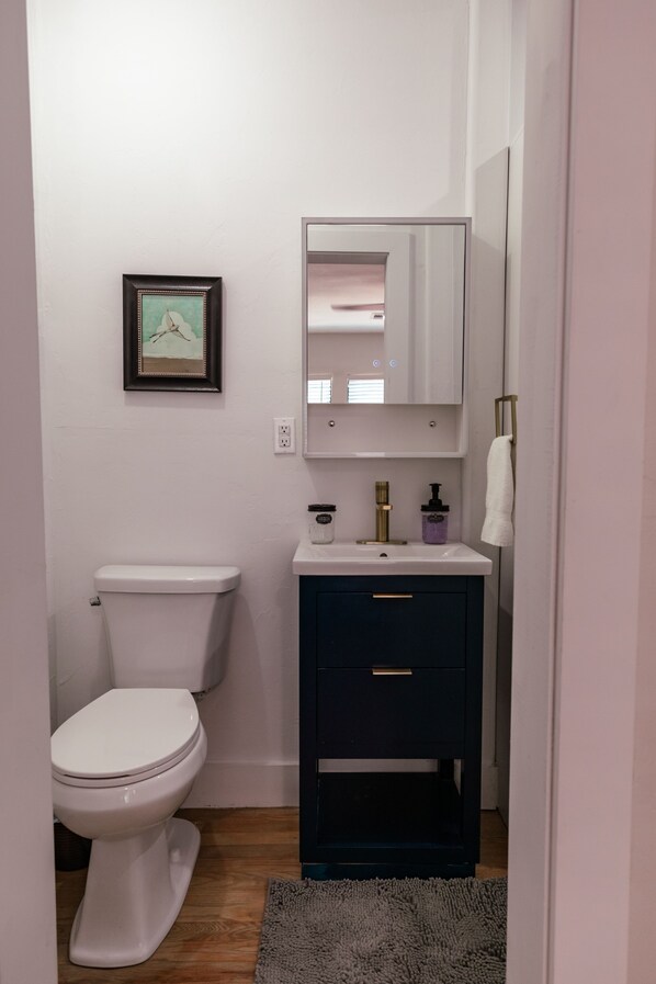 A small bathroom with a white toilet, a dark vanity with a mirror, and a framed picture on the wall. - Beautiful remodeled historical home in safe neighborhood downtown. (Oklahoma City)