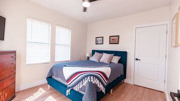 Un dormitorio con cama, cómoda, ventilador de techo y dos ventanas.