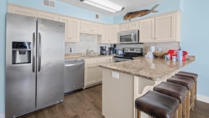 A kitchen with a stainless steel refrigerator, a microwave, a coffee maker, and a granite countertop.
