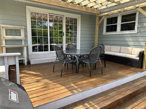 Un patio couvert avec une terrasse en bois, une table ronde entourée de chaises et un canapé.