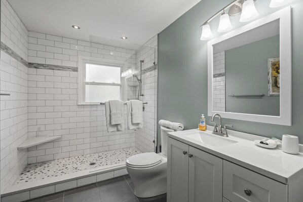 Un baño moderno con azulejos blancos tipo metro, ducha, inodoro, tocador con espejo y ventana.
