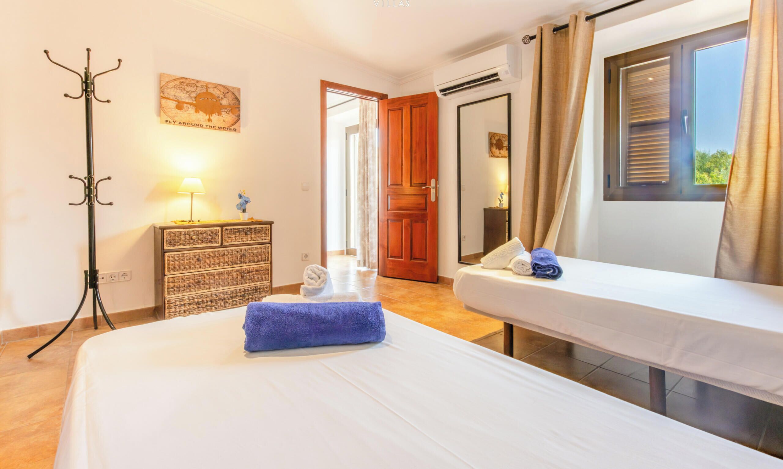 A hotel room with two beds, a wooden dresser, a lamp, and a view of the outside.