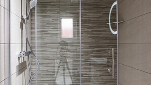 Un box de ducha moderno con puerta de cristal, un cabezal de ducha de mano y un cabezal de ducha de lluvia empotrado en la pared.