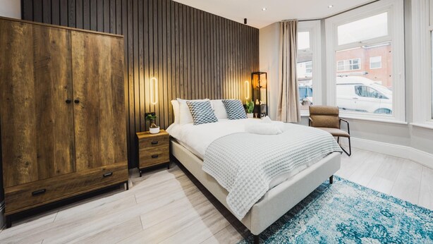 Un dormitorio moderno con una cama grande, un armario de madera, lámparas de noche y vistas a la calle a través de amplios ventanales.