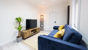 Una sala moderna con un sofá azul, un mueble de entretenimiento de madera, una planta en maceta y una lámpara de pie.