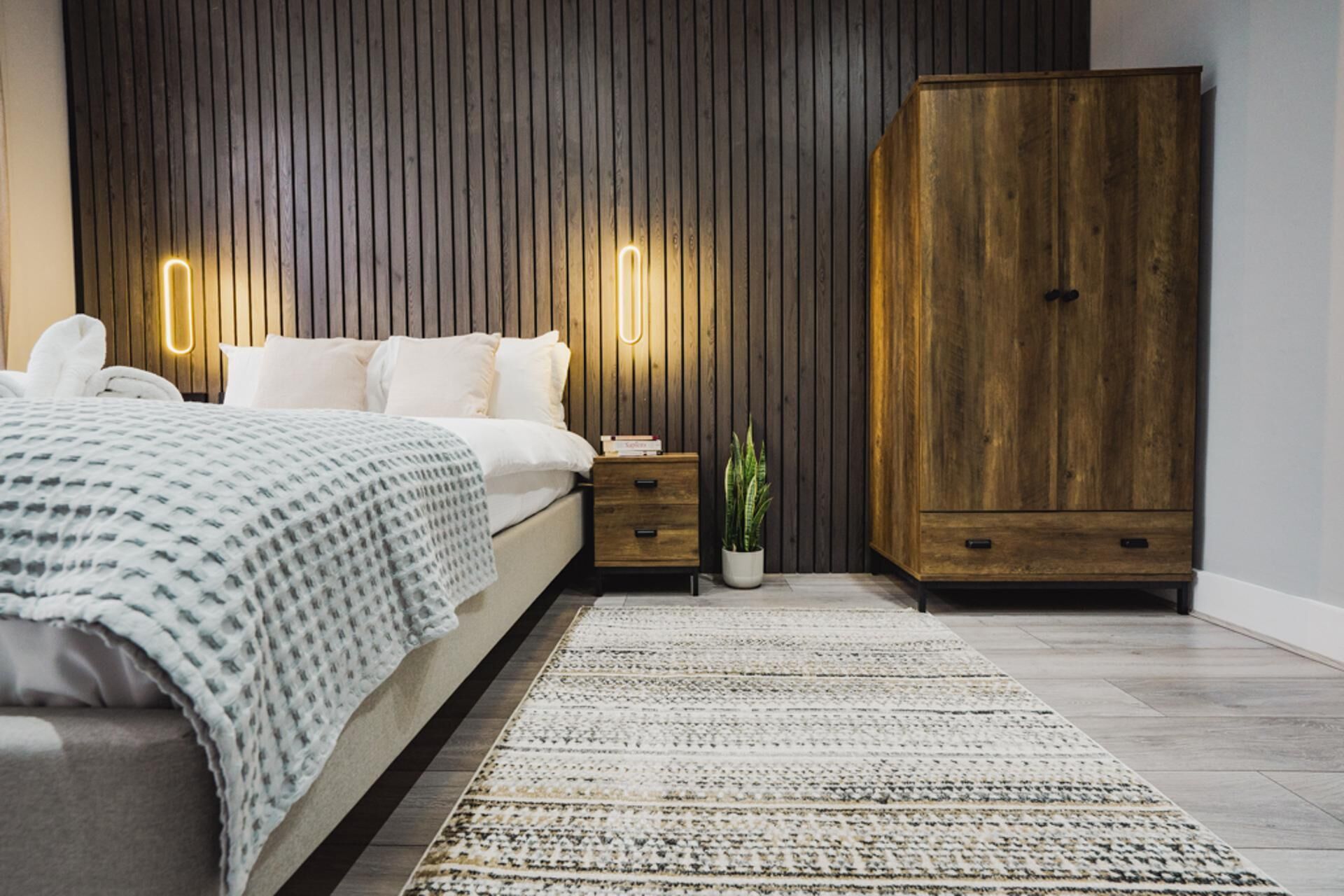 Un dormitorio moderno con cama, mesitas de noche, un armario y una planta en maceta.