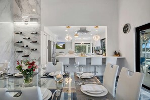 Un espace de salle à manger moderne avec un mur en marbre, des bouteilles de vin et une table en verre dressée pour un repas.