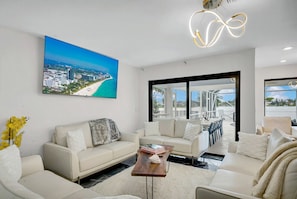 Uma sala de estar moderna com uma janela grande, um sofá, uma mesa de centro e um quadro de uma praia.