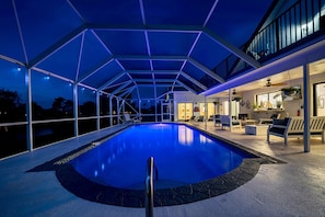 Piscina interna com estrutura de teto geométrica, área de estar e vista para o exterior.