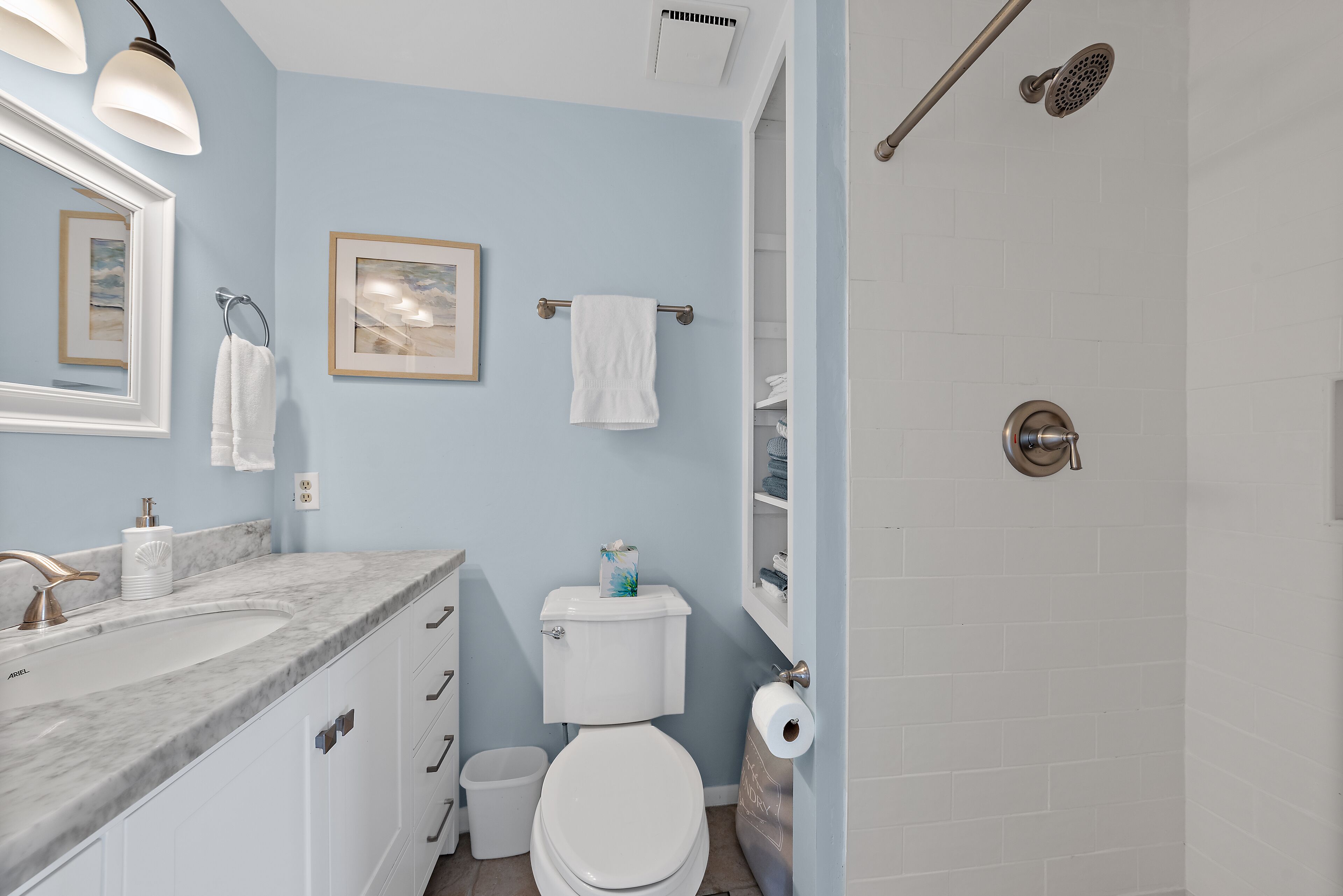 Une salle de bain avec un lavabo en marbre, des toilettes, une douche et des œuvres d’art encadrées accrochées au mur.