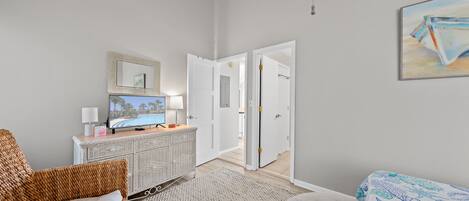 Una habitación de hotel con televisión, muebles de mimbre, un armario blanco y un cuadro en la pared.