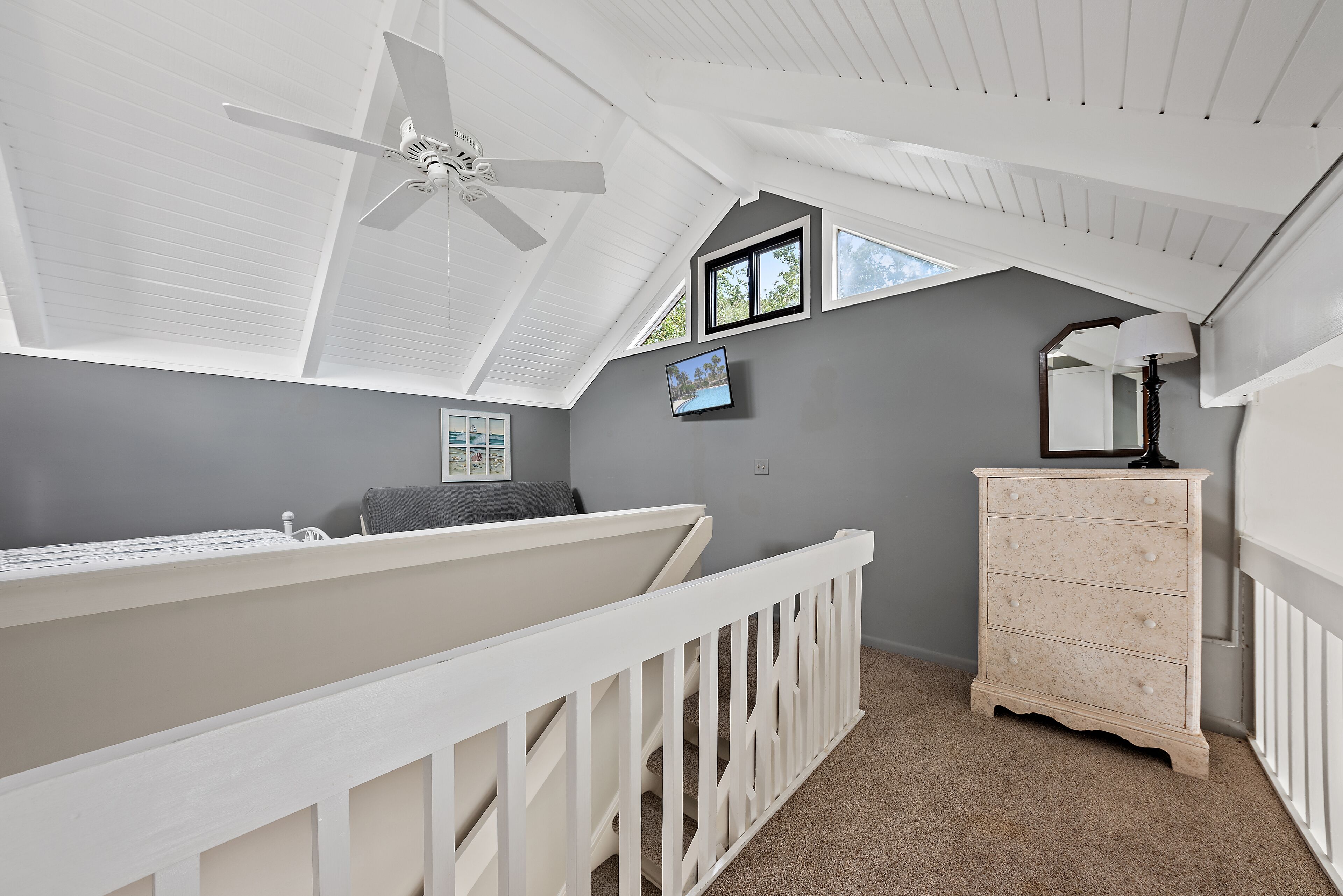 Ein Zimmer mit hohen Decken, einem weißen Deckenventilator, einem Fenster, einem Schminktisch und einem kleinen Bildrahmen an der Wand.