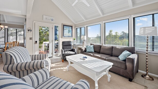 A spacious living room with a high ceiling, large windows, a ceiling fan, and a view of the outdoors. - 3BR/2BA Cottage! Close to beach! Golf Course Views! Amenity access available! (Seabrook Island)