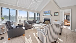 A spacious living room with a high ceiling, large windows, a fireplace, and a view of the outdoors. - 3BR/2BA Cottage! Close to beach! Golf Course Views! Amenity access available! (Seabrook Island)