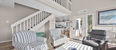 A spacious living area with a high ceiling, a staircase, and a view of the outdoors.