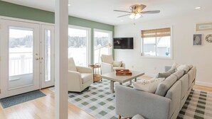 A living room with a ceiling fan, a TV, and a large window with a view of trees. - Lakefront Family Fun Retreat (Newport)