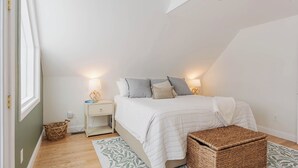 A bedroom with a bed, bedside tables, a nightstand, a woven basket, and a patterned rug. - Lakefront Family Fun Retreat (Newport)