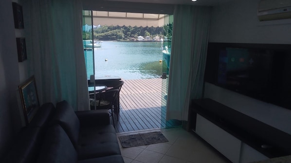 Un salon avec un canapé, un téléviseur et une porte vitrée donnant sur un balcon d’où l’on peut admirer un plan d’eau et des bateaux.