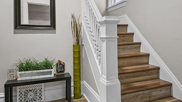 Una escalera con barandillas blancas y peldaños de madera, una consola con objetos decorativos y un espejo en la pared.