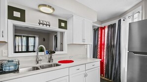 Una cocina moderna con armarios blancos, un refrigerador de acero inoxidable y un escurreplatos rojo.
