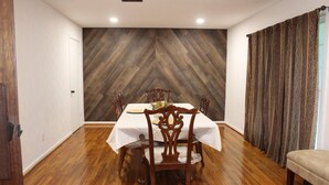 Ein Esszimmer mit Wandverkleidung aus Fischgrätparkett, einem Tisch mit weißem Tischtuch, Holzstühlen und einer Bank.