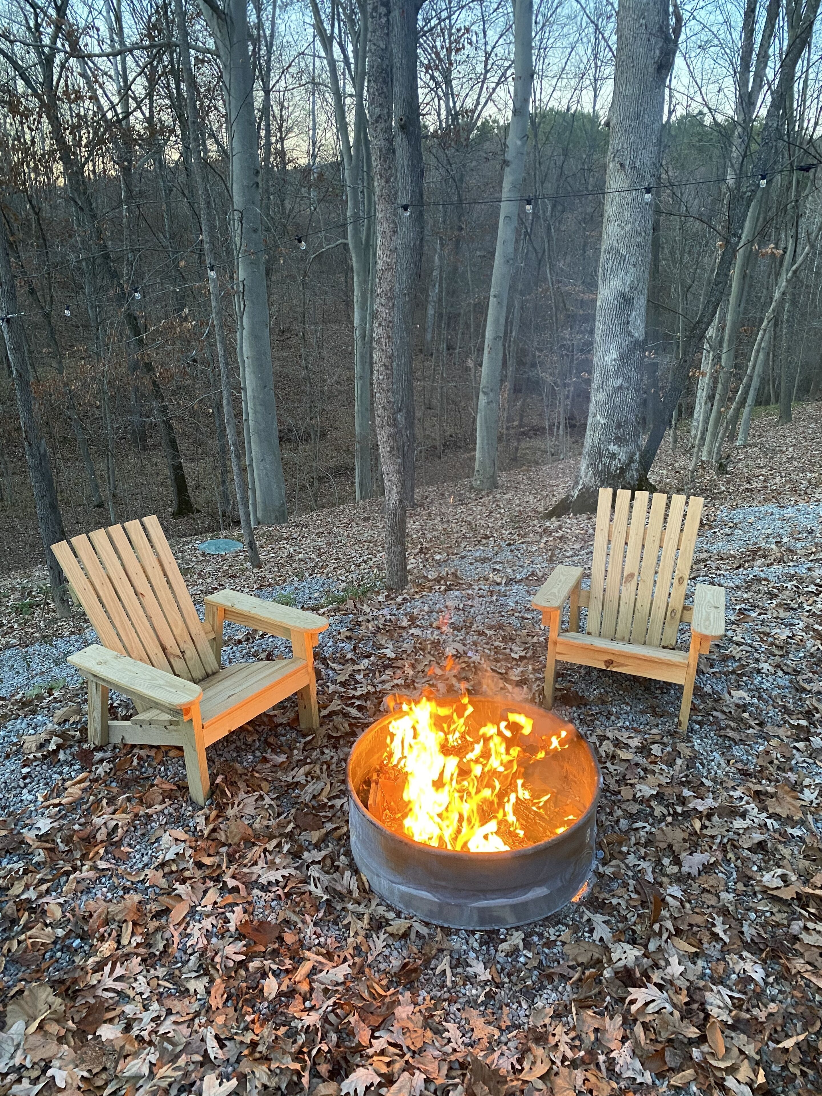 Two wooden Adirondack chairs facing a metal fire pit surrounded by dry leaves.