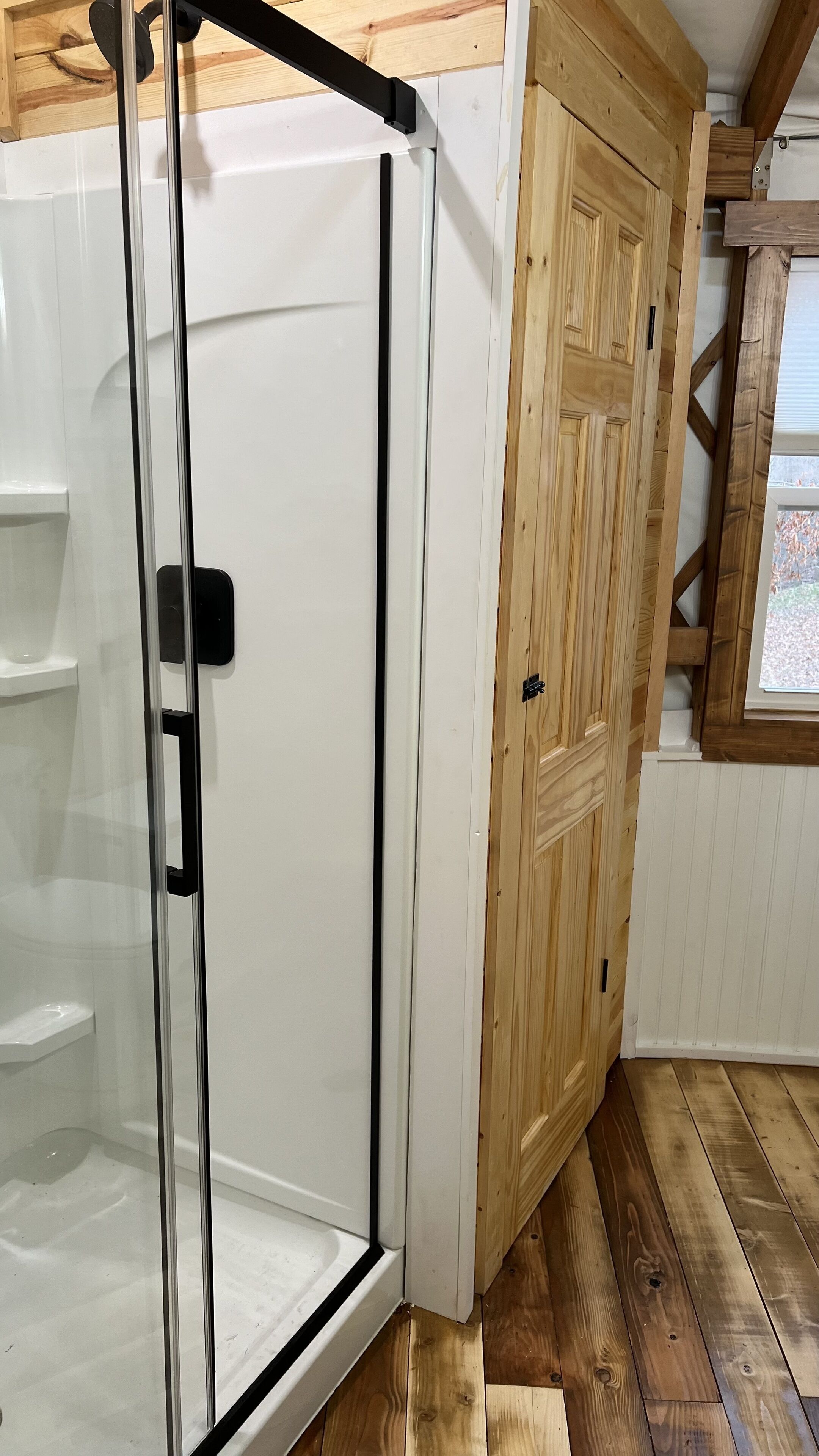Une salle de bain avec une douche à parois de verre, une porte en bois et une fenêtre.