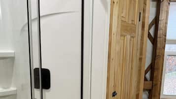 Une salle de bain avec une douche à parois de verre, une porte en bois et une fenêtre.