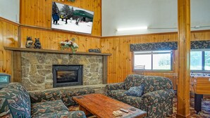 L’intérieur chaleureux d’un chalet avec une cheminée en pierre, des meubles à motifs et un téléviseur diffusant une scène enneigée.